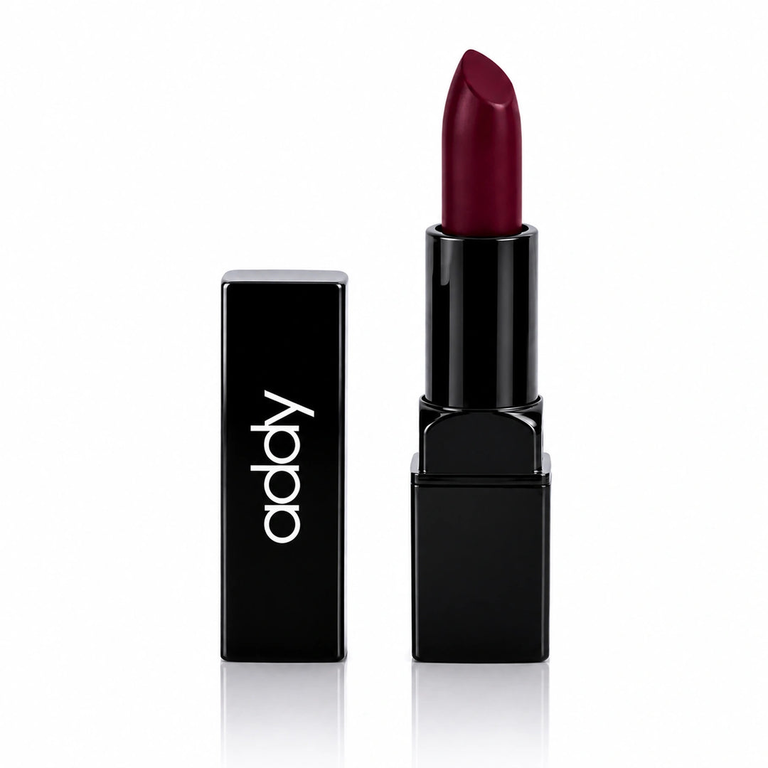 A dark red lipstick in a glossy black tube standing next to its matching black cap, which features the brand name 'addy' in white lowercase letters, set against a clean white background with a subtle reflection.